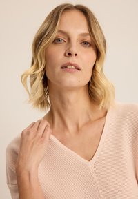 Jasnoróżowy sweter w serek z teksturowanym wzorem, z krótkimi rękawami i luźnym krojem, wykonany z miękkiego, przewiewnego materiału.