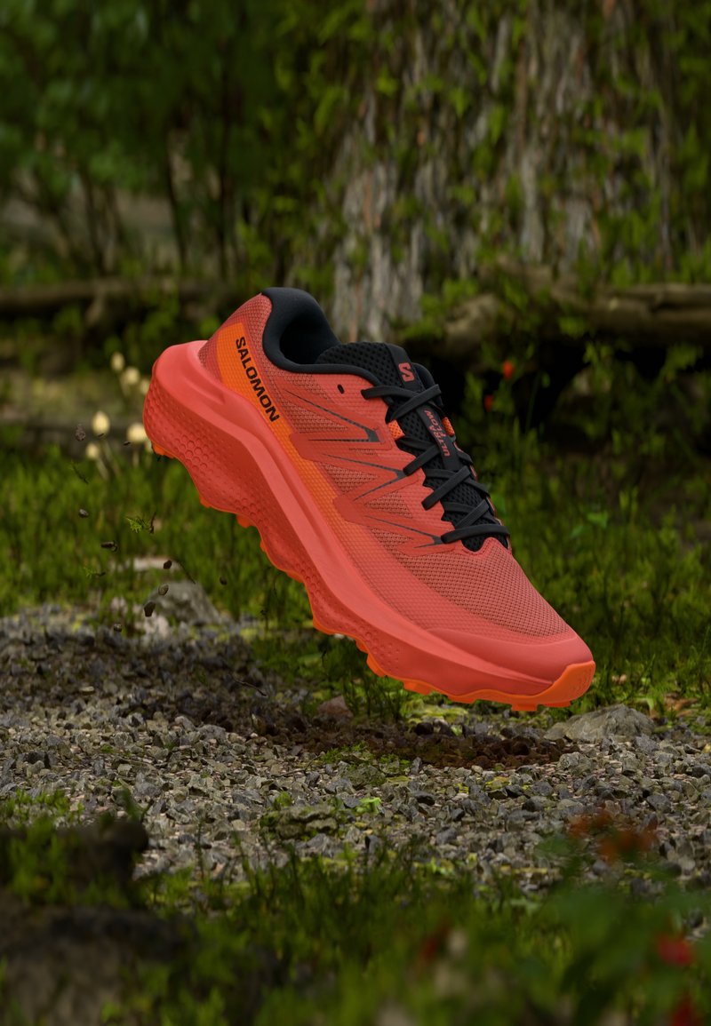 Κόκκινο αθλητικό παπούτσι με υφή διχτυού στην επάνω πλευρά, μαύρες λεπτομέρειες, έντονη ενδιάμεση σόλα με απορρόφηση κραδασμών και ορατό σύστημα κορδονιών. Εμφανίζεται το λογότυπο της μάρκας.