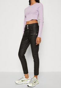 Czarne skórzane spodnie z zamkami błyskawicznymi i wysokim stanem, połączone z jasnofioletowym, krótkim topem z długim rękawem oraz wielokolorowymi trampkami.