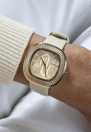 Orologio con cinturino in silicone beige, cassa quadrata in tono oro, quadrante embossato e lunetta testurizzata, che mostra il nome del marchio "Furla."