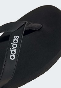 Chanclas negras con suela mate y tira texturizada. Cuenta con el logo "adidas" en blanco en la tira. Diseño simple con una forma plana y minimalist. 