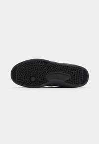 Semelle de chaussure en caoutchouc noir avec motif de bande de roulement circulaire et zones de préhension rectangulaires au talon et à l'avant du pied.