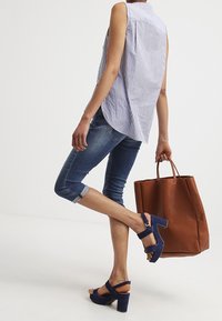 Light blue and white striped sleeveless shirt, blue jeans, navy block-heeled sandals, and a brown tote bag. Casual outfit with varied textures.