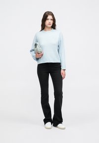 Lyseblå kort genser med lange ermer, kombinert med svarte vide jeans og hvite joggesko, holdt sammen med en grå pouch.