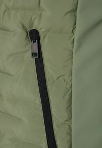 Grüne Pufferjacke mit einem schwarzen Reißverschluss. Der Stoff hat eine glatte Oberfläche mit gesteppten Mustern.