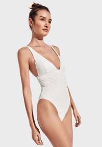 Bañador de una pieza blanco con un profundo escote en V, tirantes anchos, puntos texturizados y piernas de corte alto para una silueta elegante. Acabado de tela suave.