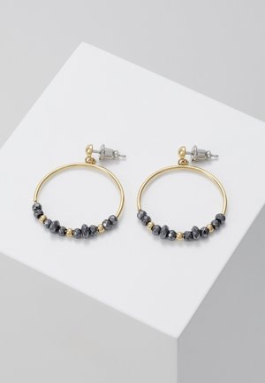 Gouden oorringen met afwisselend kleine zwarte en gouden gefacetteerde kralen op een witte schuine ondergrond.