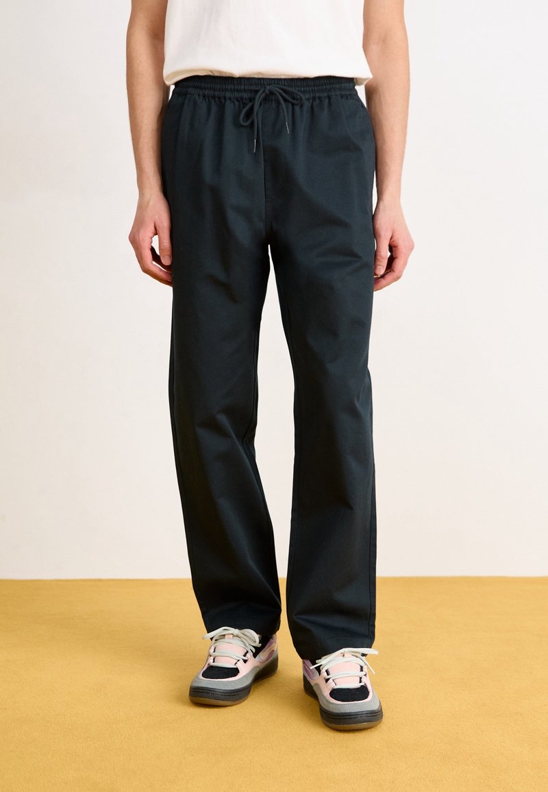 Black, lightweight, elastic waistband trousers with a relaxed fit, paired with multicolored athletic shoes featuring laces and rubber soles.