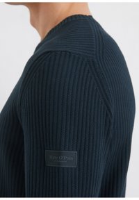 Navyblauer gerippter Strickpullover mit Rundhalsausschnitt. Verfügt über eine Schulternaht und ein Stoffetikett am Ärmel mit "Marc O'Polo"-Markenlogo.