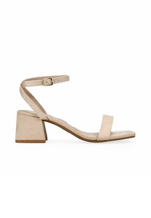 Sandalia de ante beige con punta abierta, tacón ancho, banda delantera única y correa ajustable en el tobillo con hebilla dorada.