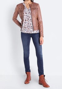 Brun läderjacka med två bröstfickor, blommig blus, mörkblå tajta jeans och bruna snörstövlar.