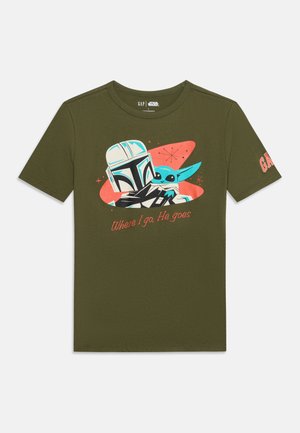 T-shirt vert foncé avec un motif Star Wars montrant le Mandalorien tenant Bébé Yoda et le texte « Where I go, He goes » sur le devant.