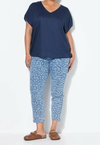 Haut bleu marine à col en V avec manches courtes, accompagné d'un jean bleu clair imprimé léopard et de chaussures marron à enfiler avec un accent de chaîne.