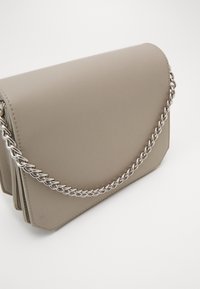 Beige syntetisk skuldertaske med en glat tekstur, der har en trekantet klap og en sølvmetalkæde som strop.