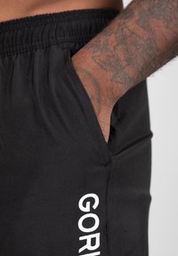 Zwarte sportieve shorts met een elastische tailleband, zijzakken en witte logo tekst op het onderbeen. Glad materiaal, strakke pasvorm.