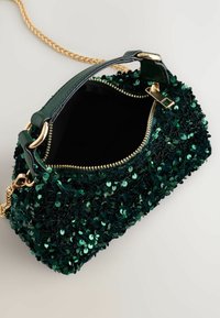 Sac à main en sequins verts avec fermeture éclair, quincaillerie dorée et une bandoulière en chaîne. L'intérieur est noir, complétant la texture et la couleur de l'extérieur.