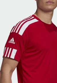 Maglietta atletica rossa con accenti bianchi a tre strisce sulle spalle. Realizzata in un tessuto leggero e liscio. Logo Adidas sul maniche.