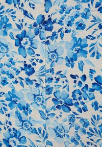 Modrá květinová tkanina s různými tvary květin a listů na světlém béžovém pozadí, se změnami odstínů modré, které zdůrazňují design.