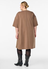 Brun oversized kjole med korte ærmer, der har en bagsøm. Et par sorte cowboystøvler med nitter og spidse tæer.