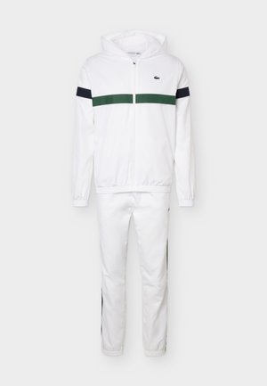 Valge lukuga kapuutsiga jakk ja sobivad püksid, jakil roheline horisontaaltriip ning varrukatel ja pükstel must triip külgedel.