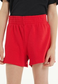 Shorts en coton rouge avec une taille élastique, présentant une coupe décontractée et une texture lisse, des bords ourlés et sans matériel ou motifs visibles.