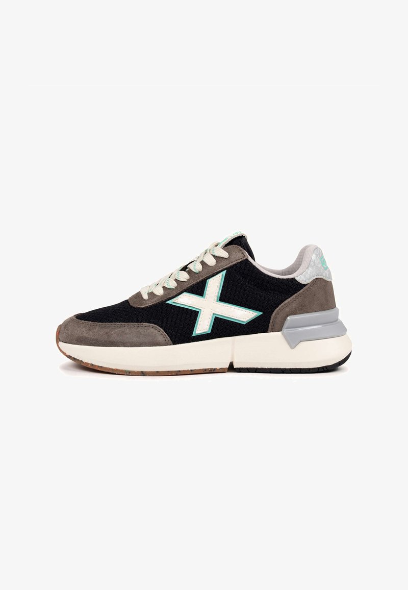 Chaussure de sport noire et grise avec une tige en mesh, des accents en daim, une semelle blanche et un logo vert menthe. Elle présente un tissu texturé et des lacets plats.