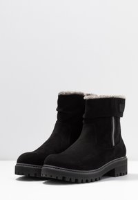 Bottines en daim noir avec un revers replié, une bande grise en accent, une semelle épaisse en caoutchouc et une doublure texturée pour un confort accru.