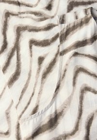 Lättviktig tyg med ett beige och mörkbrunt vågigt zebramönster, med en sidoficka och slät textur.