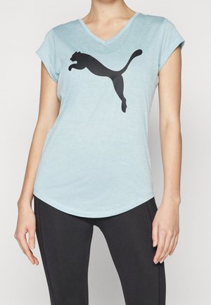 Kvinde iført en lyseblå T-shirt med V-udskæring og stort sort Puma-logo, kombineret med sorte tætsiddende træningsleggings.