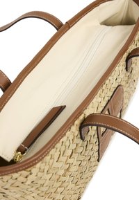 Sac cabas en paille tissée avec des accents et des anses en cuir marron ; intérieur crème avec une poche zippée et une poche plate.