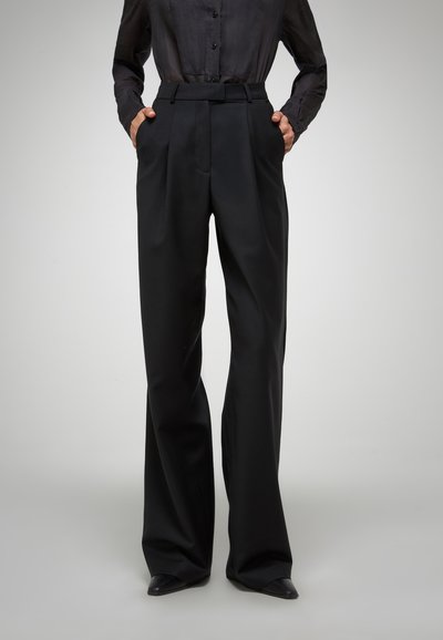 Pantalons noirs taille haute avec une coupe ajustée, présentant une taille plate et des poches latérales, en tissu lisse avec un léger éclat.