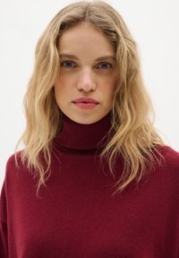 Pull à col roulé bordeaux en tissu tricoté côtelé doux, avec une coupe ample et une texture subtile.