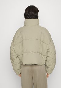 Padded jacket in light beige, featuring a high collar, oversized silhouette, quilted texture, and soft material. Seam details visible.