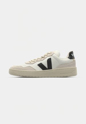 White and beige leather sneaker with black logo. Features suede accents, round toe, lace-up front, and textured rubber sole.