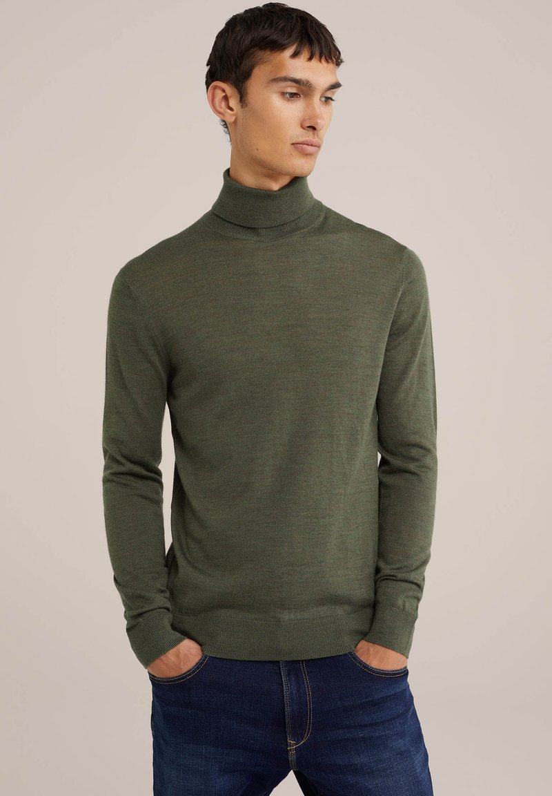 Pulover cu guler înalt de culoare verde măslin, realizat dintr-un material moale; croială slim fit cu manșete și guler plisat; purtat peste blugi blue.
