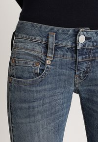 Jeans i mörkblå denim med en urtvättad yta, med fem fickor, synlig sömnad och en knappstängning fram.