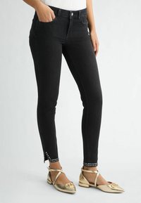 I jeans skinny neri in denim presentano un alto vita, tasche laterali e dettagli borchiati alla caviglia. Abbinati a scarpe flat dorate.