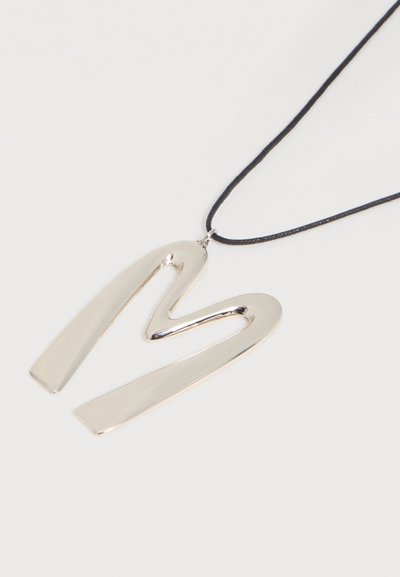 Pendentif en argent en forme de zigzag abstrait sur un collier en cordon noir fin sur fond blanc.