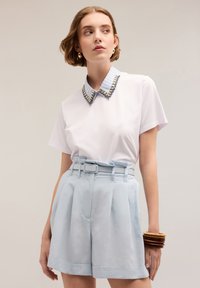 Tricou alb cu guler cu dungi, având embellismente, asociat cu pantaloni scurți ușor albaștri, cu talie înaltă și brățări stratificate.