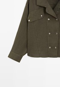 Veste boutonnée vert olive avec manches longues, poche poitrine à rabat et boutons-pression argentés à l’avant et sur le rabat de la poche.