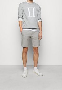 Szara bluza z nadrukiem "II", jasnoszare spodenki oraz białe trampki. Swobodny strój o luźnym kroju i podwiniętych rękawach.