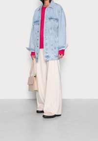 Ljusblå denimjacka med framfickor, knallrosa stickad tröja, krämfärgade vida byxor och en liten beige handväska. Skor med svarta sulor.