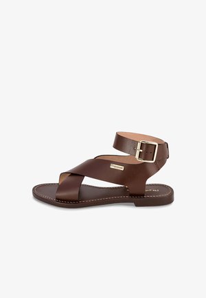 Sandale en cuir marron avec un design à lanières croisées, boucle à la cheville, semelle plate et surpiqûres contrastées pour plus de détails.