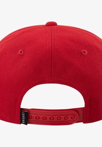 Red fabric cap with a smooth finish, featuring a curved brim and an adjustable snapback closure. Two ventilation holes on the top.