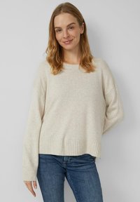 Hellbeiger Strickpullover mit lockerem Schnitt, gerippten Bündchen und Saum. Hergestellt aus weichem Stoff mit dezentem Muster. Kombiniert mit dunkler Jeans.