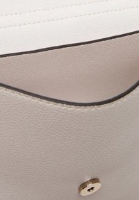 Interno di borsa in pelle beige chiaro con superficie strutturata, forma arrotondata, cuciture scure a contrasto e dettaglio di chiusura a scatto dorata.