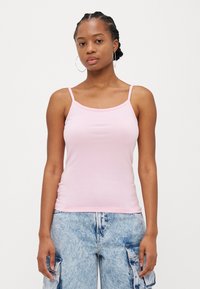 Lys rosa bomullstank topp med tynne stropper og rund hals, brukt sammen med lyse blå cargo bukser. Glatt tekstur, tettsittende design.
