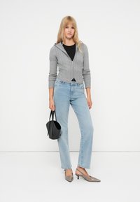 Pelēks kapuci kardigans ar kabeli adījumu, melna krekls, gaiši zili taisnas kājas džinsi, pelēki slingback apavi un mazs melns rokassomu.