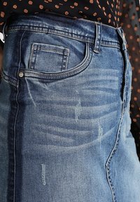 Farkkuhame, jossa on vaaleansininen pesu, hienovaraista kulutusta, kuluneita yksityiskohtia ja klassinen viisi taskua -malli metallinapeilla.