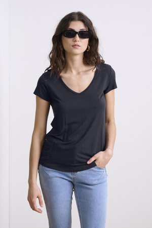 Un t-shirt noir à col en V fabriqué en tissu doux et lisse, associé à un jean bleu clair. Le t-shirt présente des manches courtes et une silhouette ajustée.